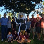 Augsburg Alumni gather around Auggie Eagle standup in a park in Rochester